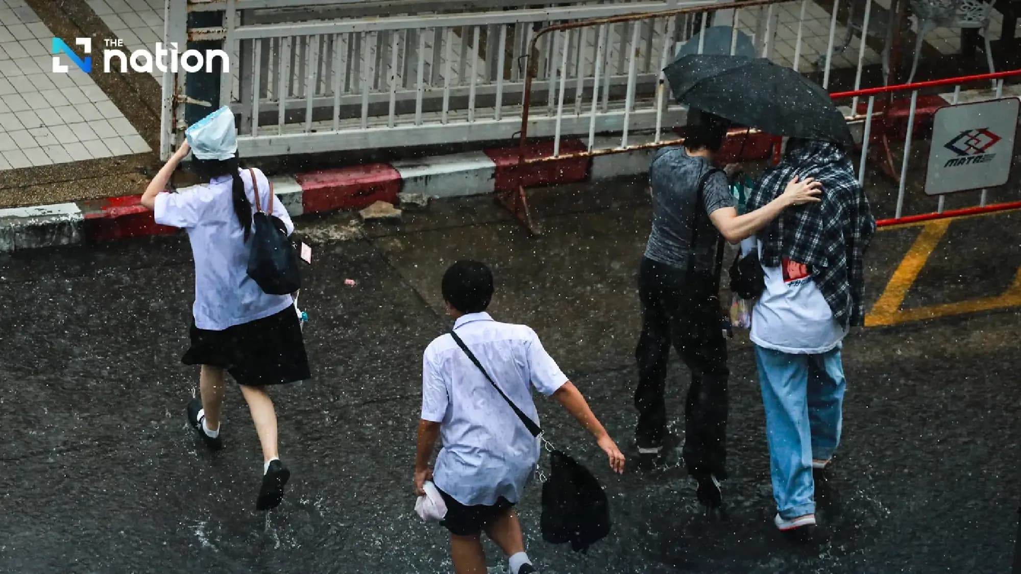 People walking through heavy rain on a street in Thailand, reflecting the immediate impact of Tropical Storm Wipha's widespread downpours.
