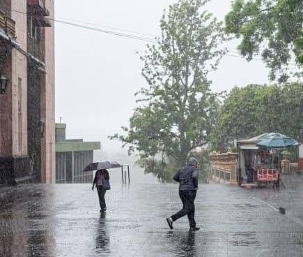 People walking with umbrellas on a misty, wet street in Xalapa, reflecting the city's unique cloudy climate.