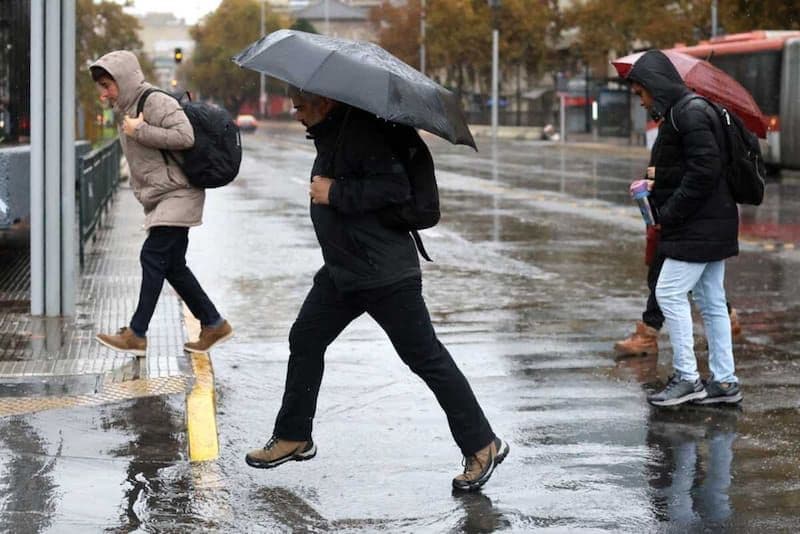 People walking with umbrellas on a wet street in Santiago during winter rain, symbolizing the city's anticipation for precipitation.