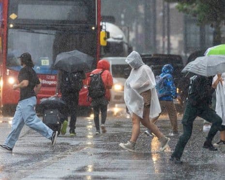People with umbrellas and raincoats navigate a flooded urban street in heavy rain, depicting Britain's urban flood challenge.
