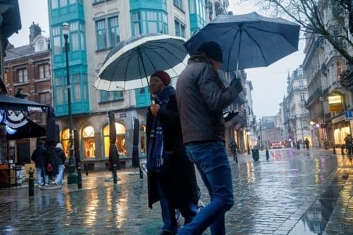 People with umbrellas on a wet city street during a summer storm, reflecting capricious weather.