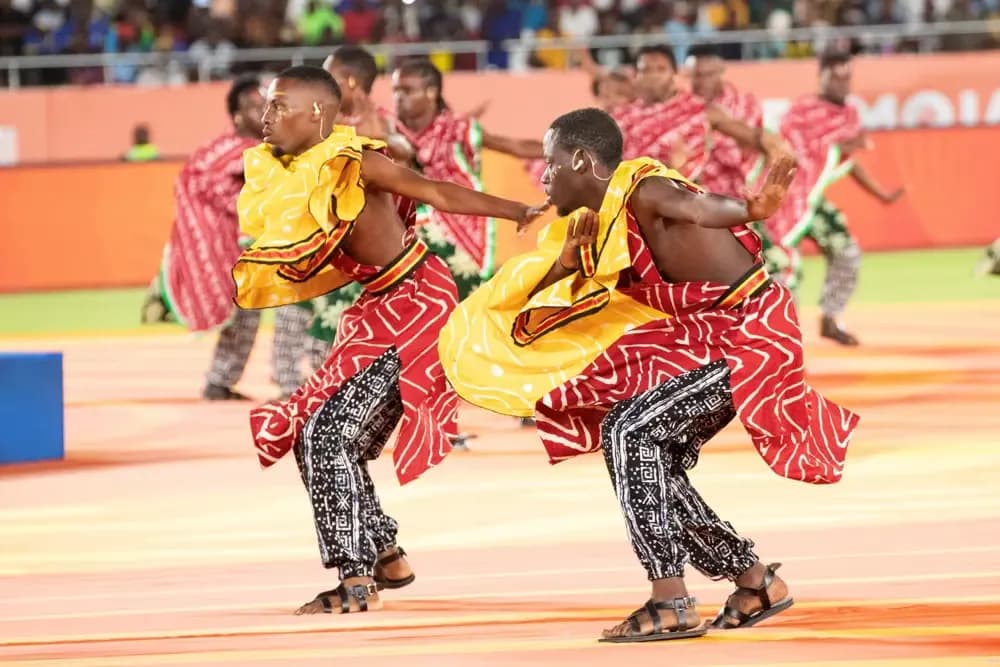 Performers in vibrant traditional attire dancing on a stadium pitch during the CHAN 2025 opening ceremony, symbolizing East African collaboration.