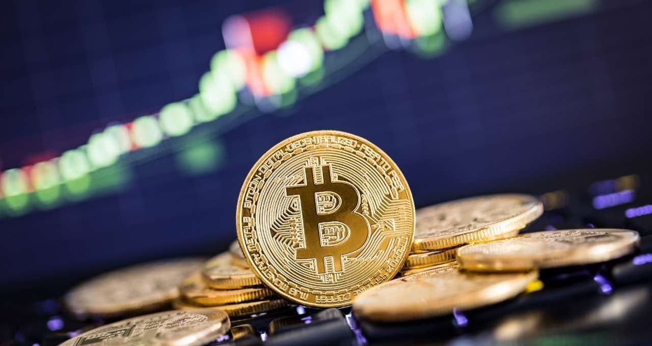 Pièces de Bitcoin dorées sur un clavier d'ordinateur avec un graphique boursier vert en arrière-plan, symbolisant la croissance du marché des cryptomonnaies.
