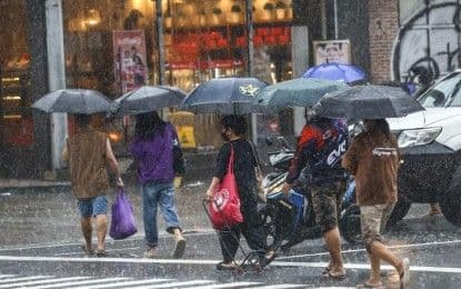 Piétons bravant la pluie intense dans une rue de Manille, illustrant l'impact des intempéries sur le quotidien.