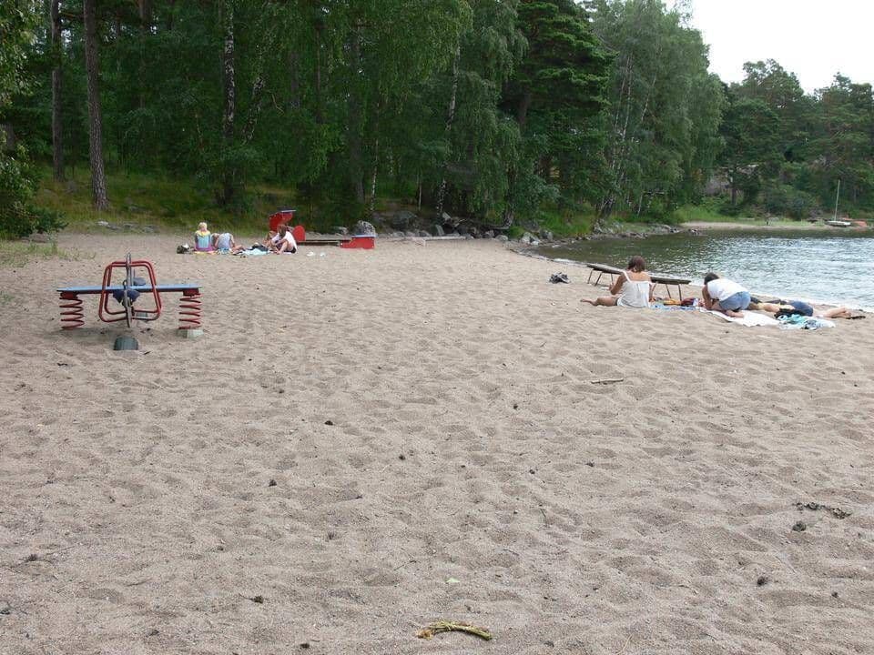 Plage de sable finlandaise avec des baigneurs et des arbres en arrière-plan, représentant les lieux de baignade.