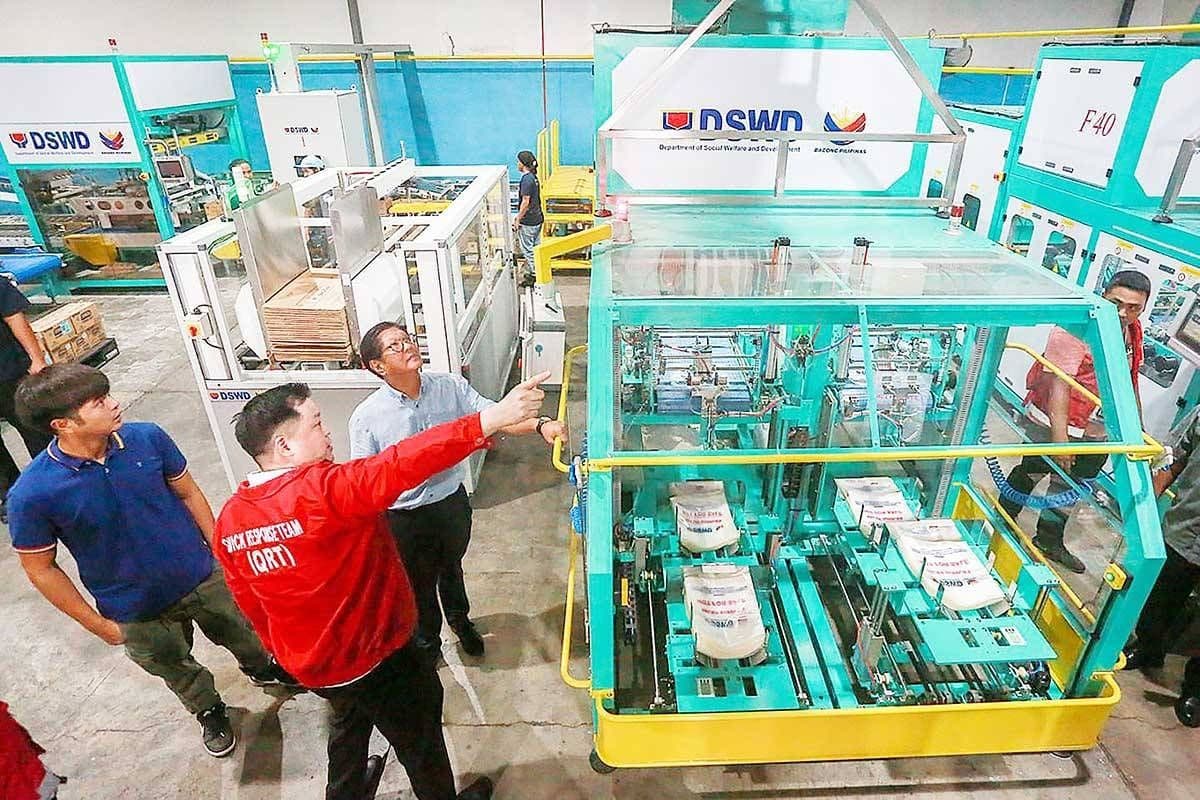 President inspecting automated repacking of relief goods at a DSWD warehouse, demonstrating crisis management and preparedness for affected communities.
