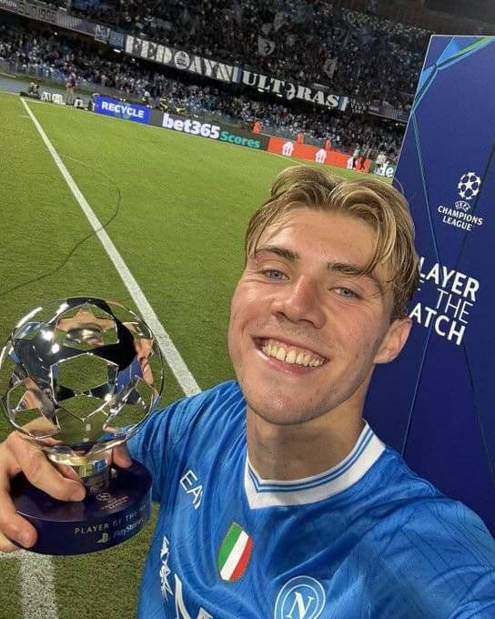 Rasmus Højlund smiling in his Napoli kit, holding the Champions League Player of the Match trophy on the pitch.