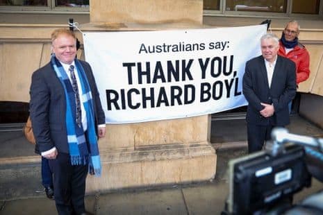 Richard Boyle et Rex Patrick devant le tribunal, avec une bannière de soutien 'Merci Richard Boyle'.