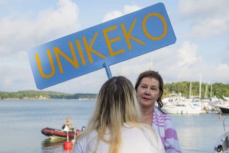 Sari Mäkiranta, l'Unikeko officiel, posant avec un panneau 'UNIKEKO' près du port de plaisance de Naantali.