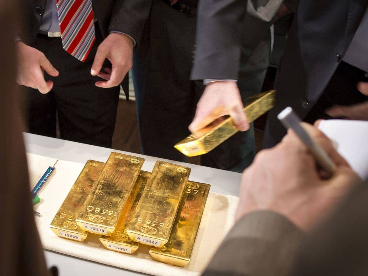 Several gold bars displayed on a table with financial professionals observing, representing the gold market in search of meaning and new anchors.