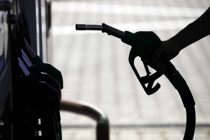 Silhouette d'une main tenant un pistolet de pompe, évoquant les forces invisibles et l'incertitude des prix du carburant.