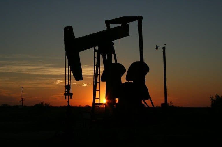 Silhouette d'une pompe à pétrole au coucher du soleil, représentant la production de brut et les ajustements de quotas de l'OPEP+.