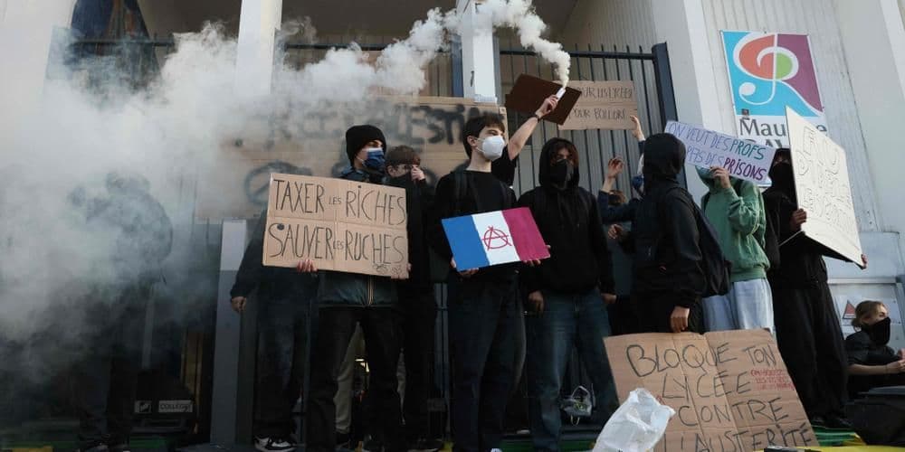 Students block a high school entrance with smoke and protest signs, symbolizing France's 'Bloquons tout' movement and its intent for disruption.