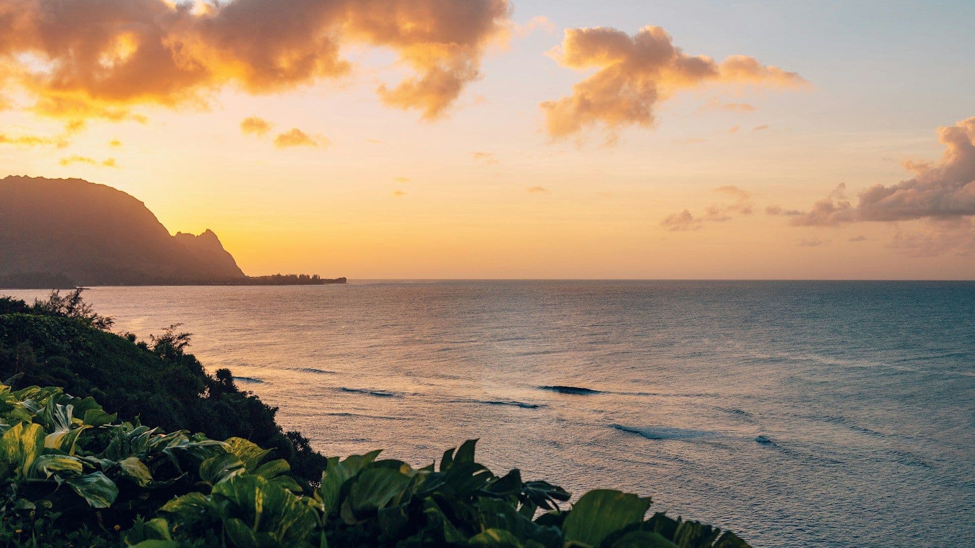 Sunset over a calm ocean with distant mountains and clouds, illustrating the vastness where global wind patterns shape weather.