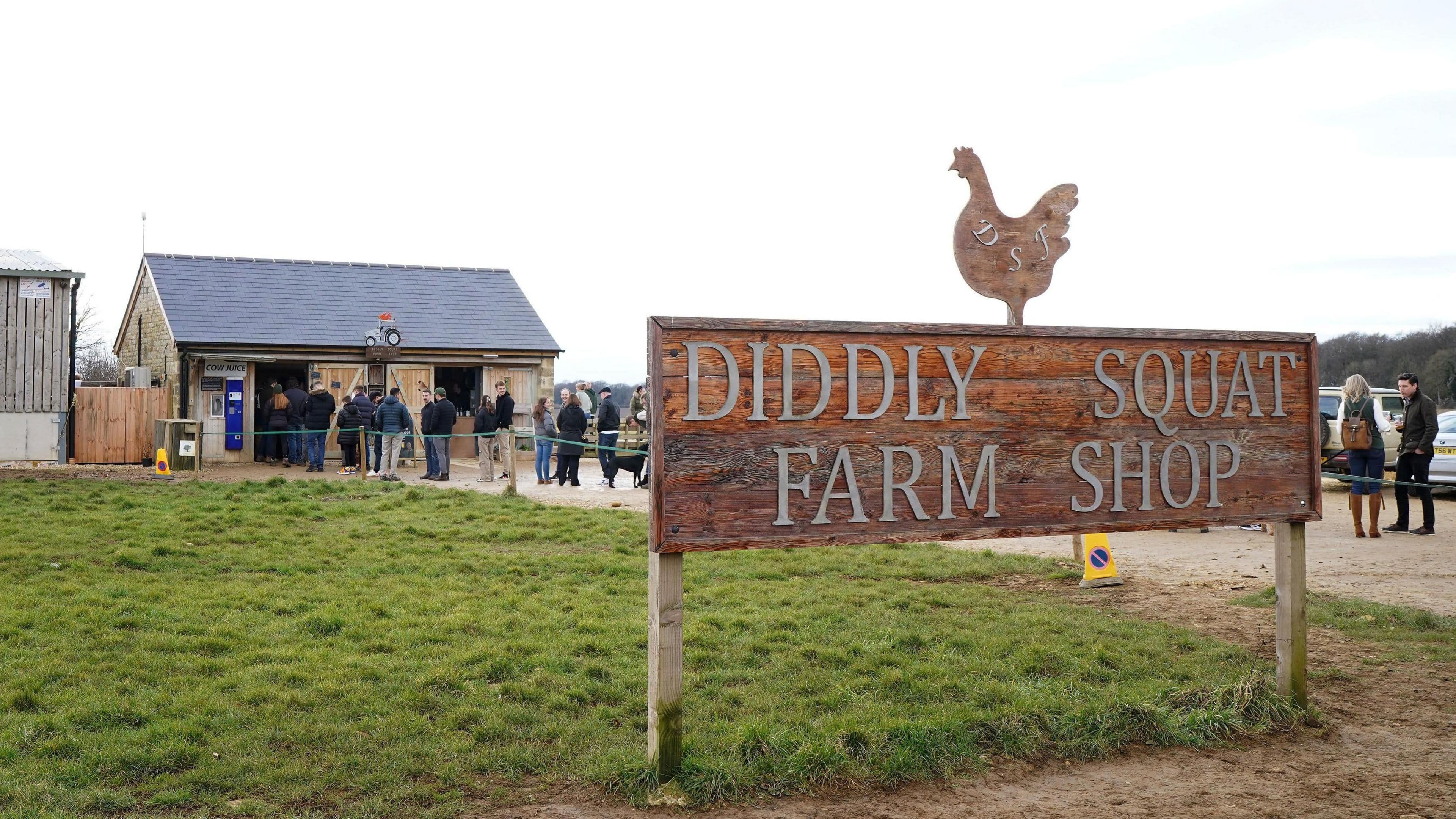 The Diddly Squat Farm Shop sign with people queuing, symbolizing the farm's enduring spirit and public presence.