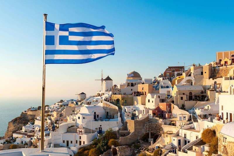 The Greek flag flying over a white village, symbolizing international water policy discussions relevant to Morocco's water scarcity challenges.