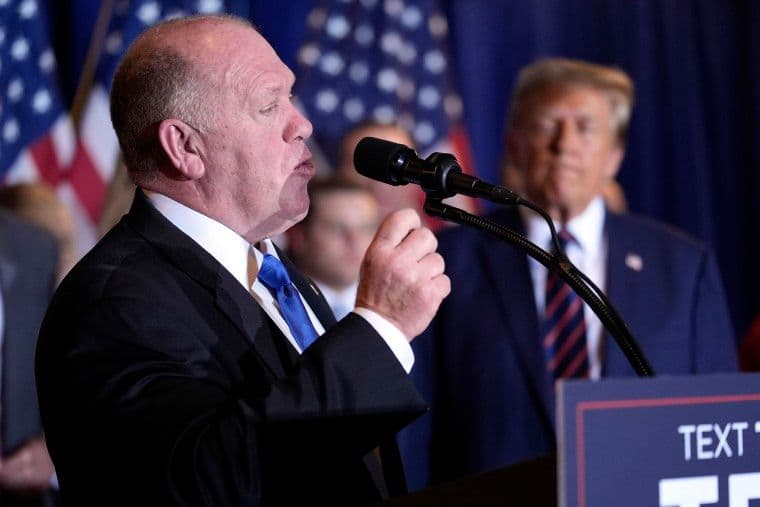 Tom Homan speaks at a podium with Donald Trump in the background, symbolizing the political context of the corruption probe.