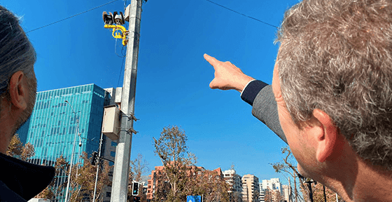 Two officials pointing towards a traffic light and camera system during a pilot presentation for Chile's Ley CATI road safety initiative.