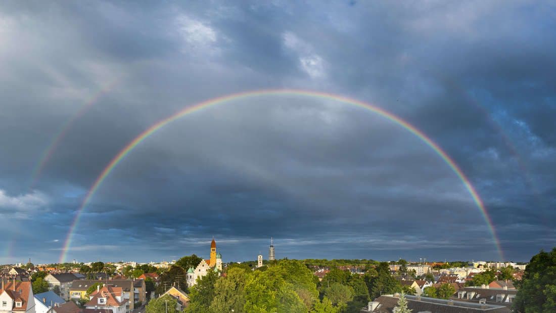 Un arc-en-ciel complet au-dessus d'une ville après une averse, symbolisant l'évolution et l'imprévisibilité du climat estival.