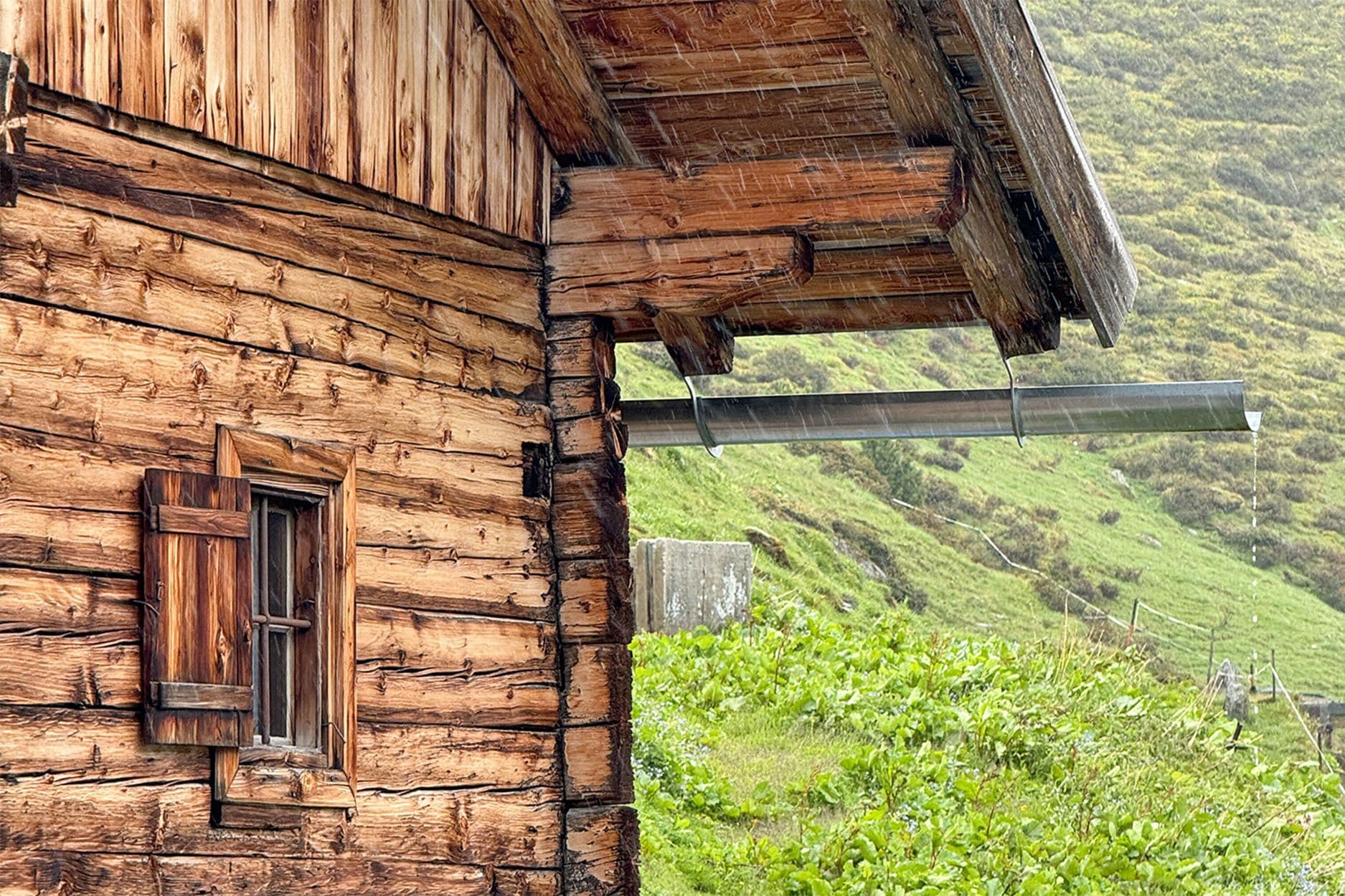 Un chalet alpin en bois sous la pluie battante, illustrant les dégâts causés par les inondations au Tyrol.