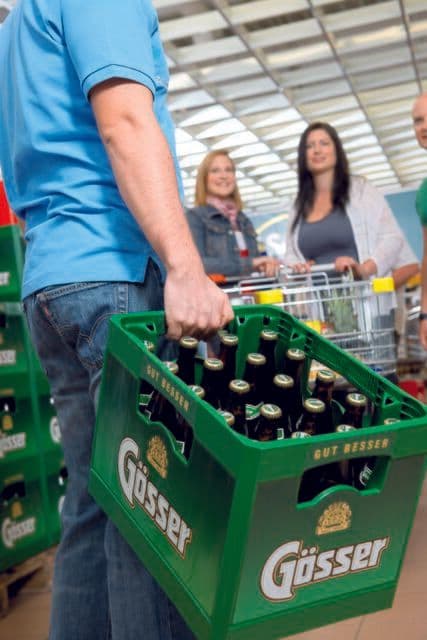 Un consommateur portant une caisse de bière dans un supermarché, symbolisant les produits alimentaires sous surveillance.