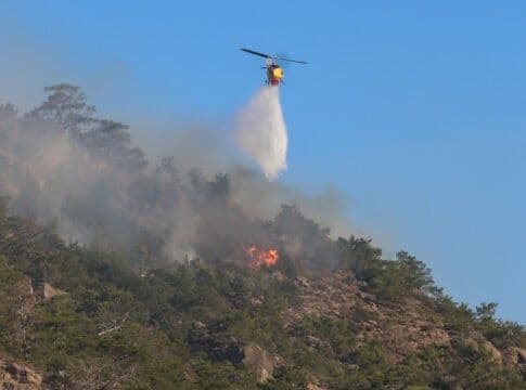 Un hélicoptère larguant de l'eau sur un incendie de forêt en Grèce, illustrant les défis climatiques et la résilience.