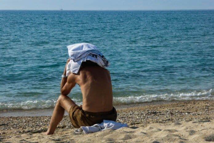Un homme assis sur une plage grecque, regardant la mer, évoquant la détente et la découverte des paysages côtiers de Thessalie ou d'Évros.
