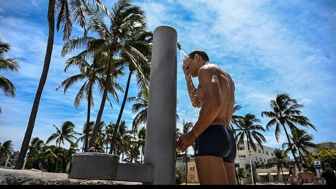 Un homme se rafraîchissant sous une douche extérieure à Miami Beach, illustrant les stratégies pour faire face à la chaleur extrême.
