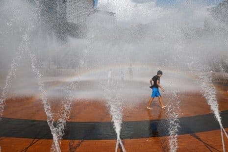 Un jeune garçon se rafraîchissant dans une fontaine publique, symbolisant l'adaptation aux conditions de chaleur extrême.