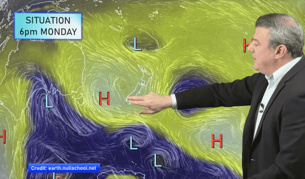 Un présentateur météo devant une carte des vents et pressions au-dessus de la Nouvelle-Zélande.