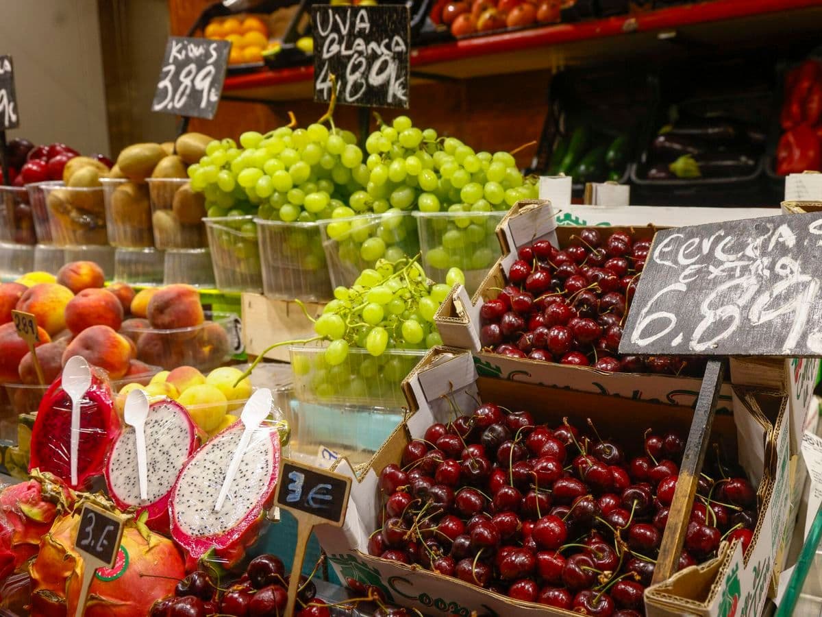 Un étal de marché coloré avec des fruits et des prix affichés, représentant l'impact direct de l'IPC sur les dépenses quotidiennes des consommateurs.