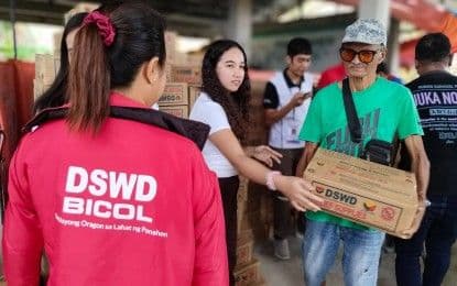 Un travailleur du DSWD distribuant des colis de secours, représentant l'aide économique et sociale déployée face aux inondations.