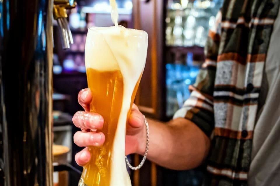 Une bière blonde débordante de mousse est versée d'un robinet, illustrant l'art, la science et la passion de la bière.