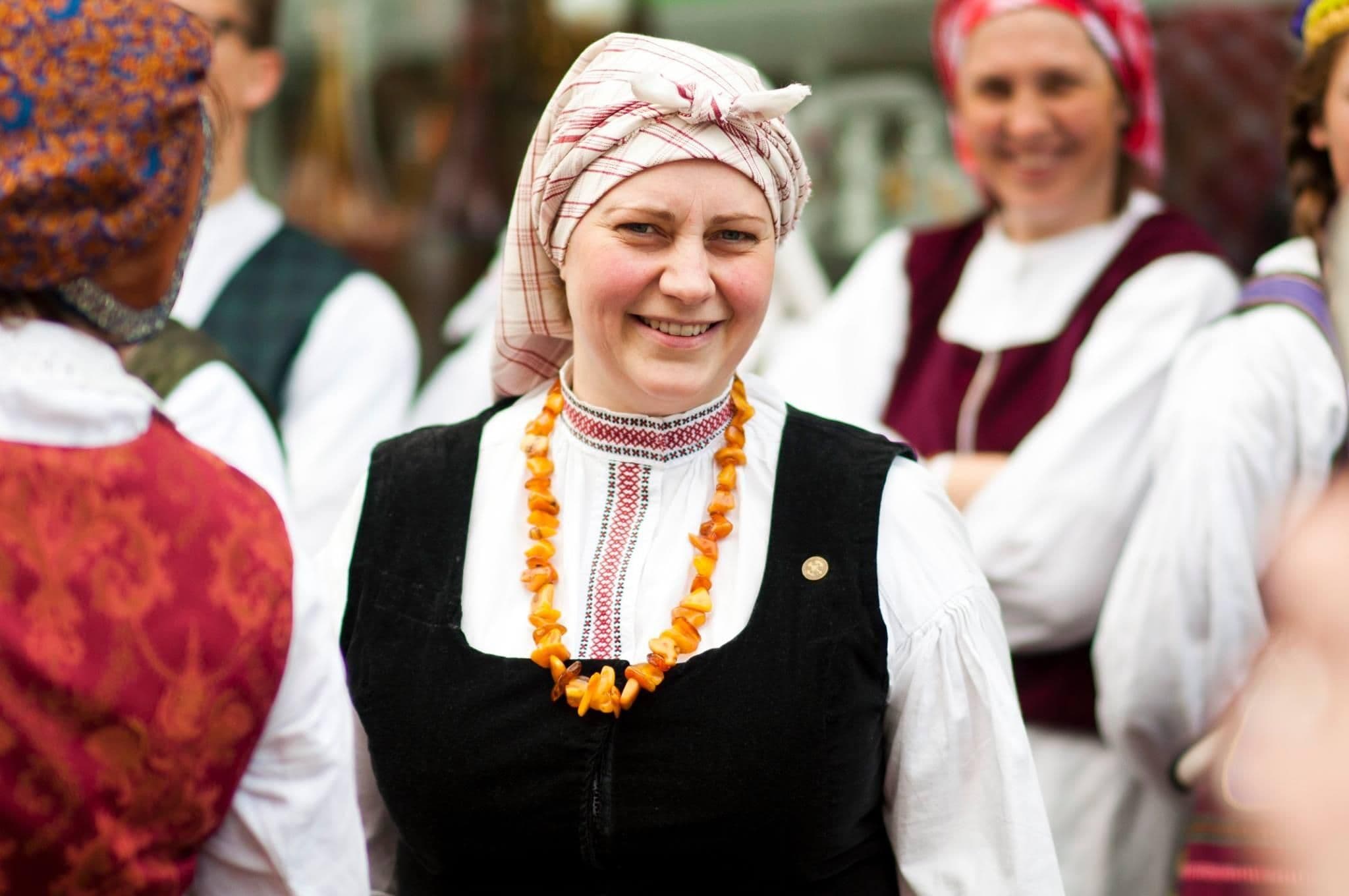 Une femme lituanienne souriante en costume traditionnel, évoquant le rituel du pain fait maison.