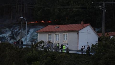Une ligne de feu visible sur une colline boisée à Ponteceso au crépuscule, menaçant les habitations.