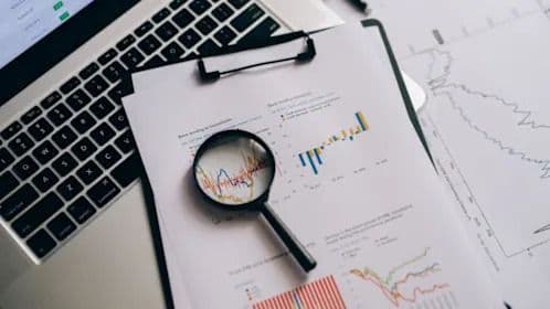 Une loupe posée sur un graphique financier à côté d'un ordinateur portable, illustrant l'analyse stratégique de Nanya Technology comme baromètre de l'industrie technologique.