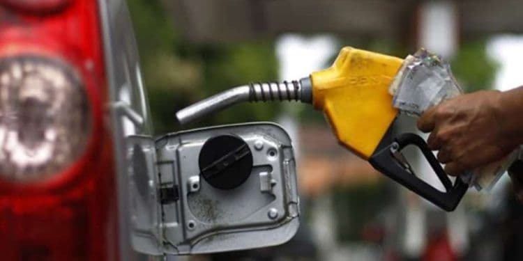 Une main tenant un pistolet de pompe à essence avec des billets de banque, symbolisant le coût et les taxes sur le carburant au Ghana.