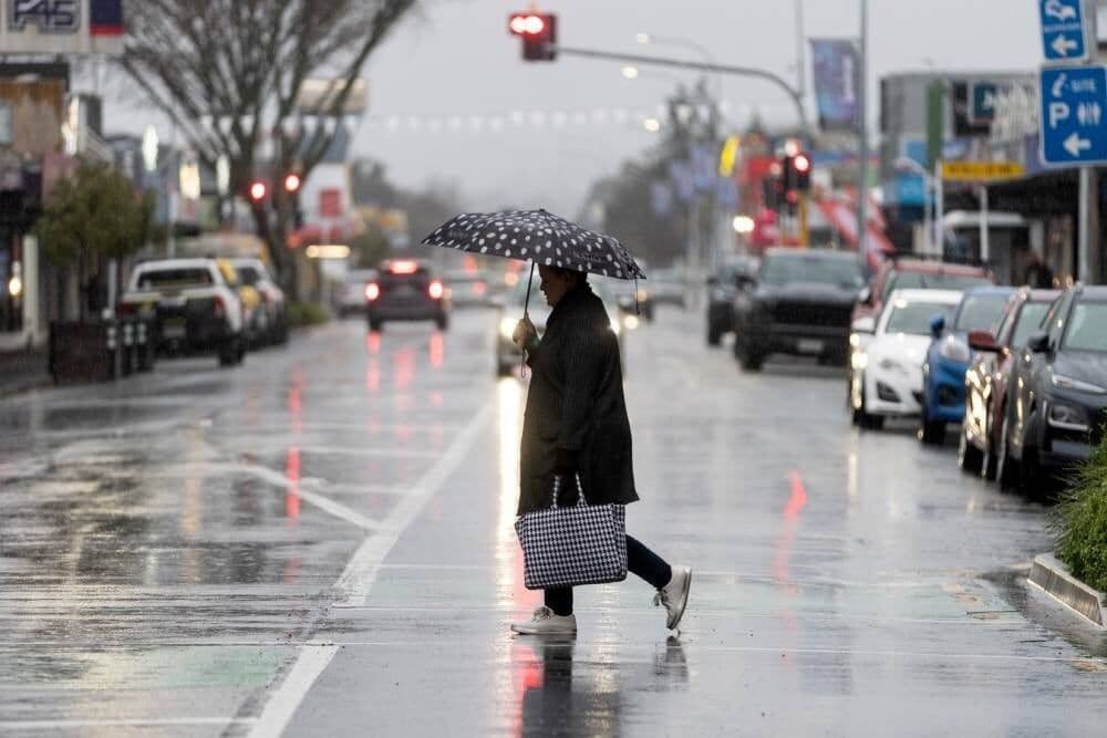 Une personne marchant sous la pluie avec un parapluie dans une rue inondée de Nouvelle-Zélande.