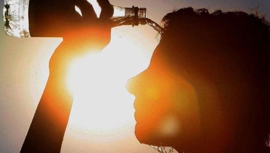 Une personne se rafraîchissant en versant de l'eau sur sa tête sous un soleil intense, symbolisant la canicule à Almaty.