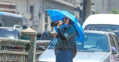 Une personne sous un parapluie bleu, buvant d'une bouteille d'eau, illustrant les mesures de protection et d'hydratation contre la chaleur extrême.
