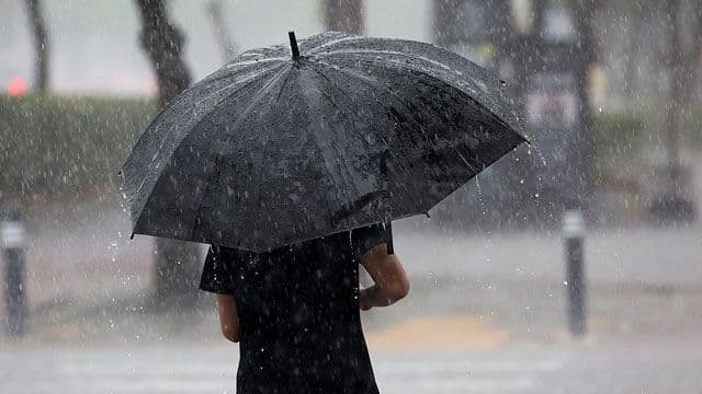 Une personne sous un parapluie noir sous une forte pluie, symbolisant l'imprévisibilité de la météo.