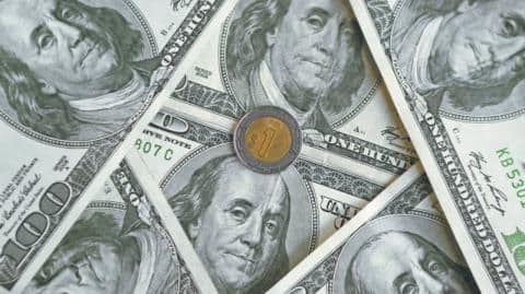 Une pièce de peso mexicain sur des billets de dollar américain, illustrant l'impact des politiques publiques sur la stabilité économique.