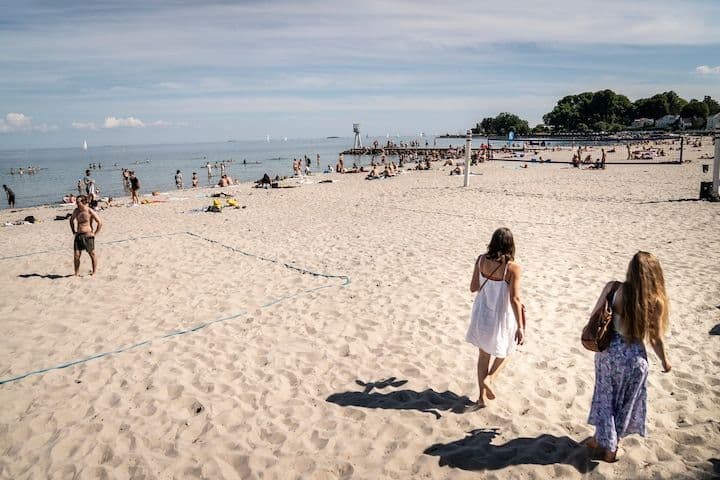 Une plage danoise ensoleillée avec des baigneurs et des personnes se relaxant sur le sable, illustrant la douceur de l'été prolongé.