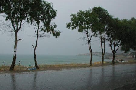 Une plage grecque sous une pluie battante et un ciel gris, symbolisant la métamorphose brutale de l'été en intempéries.