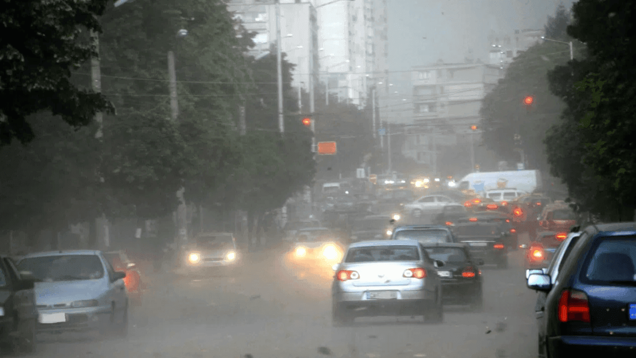 Une rue de ville balayée par une forte tempête de grêle, avec des voitures et des arbres sous la pluie et la glace.