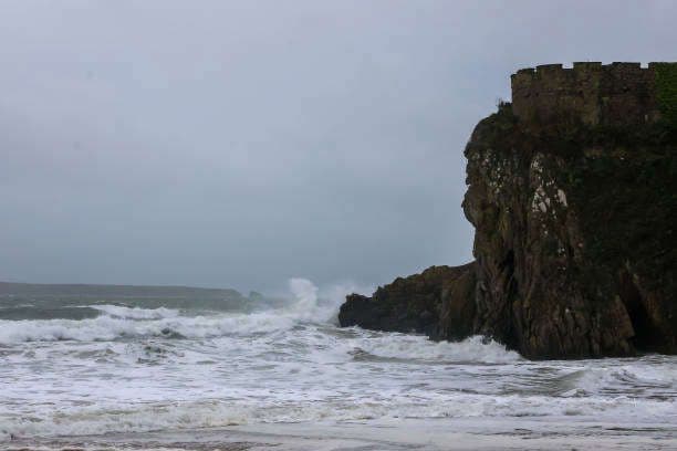 Vagues déferlantes s'écrasant sur une côte rocheuse avec un ancien château sous un ciel orageux.