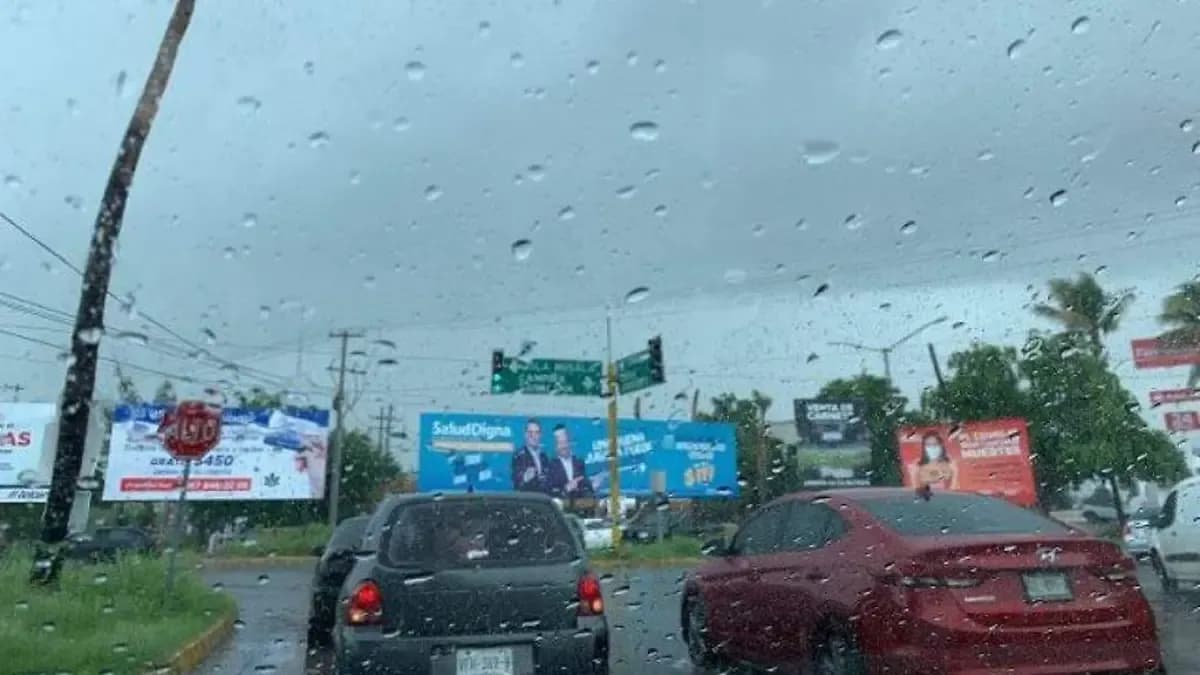 View through a rain-streaked car windshield on a Culiacán street during a heavy downpour.