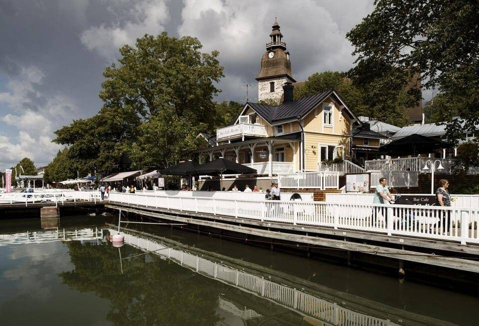 Vue panoramique du front de mer de Naantali avec ses bâtiments historiques, son clocher et ses bateaux, reflétés dans l'eau.