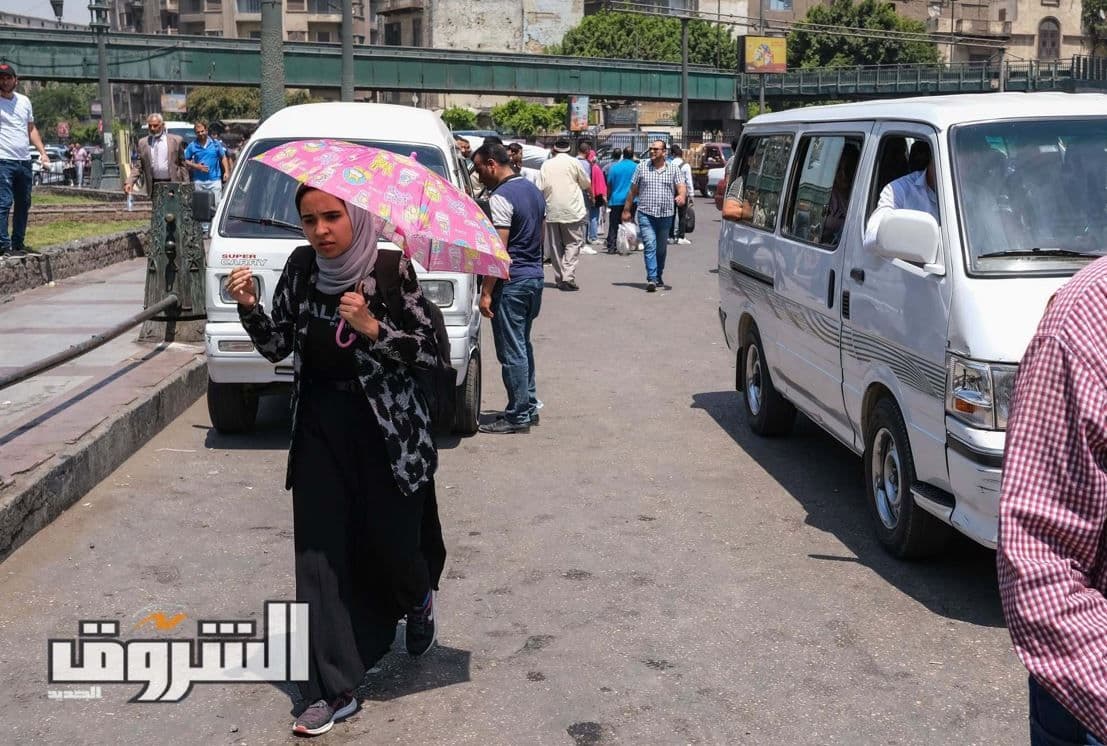 Woman walking with an umbrella for shade on a hot, sunny street in Egypt during a heatwave.