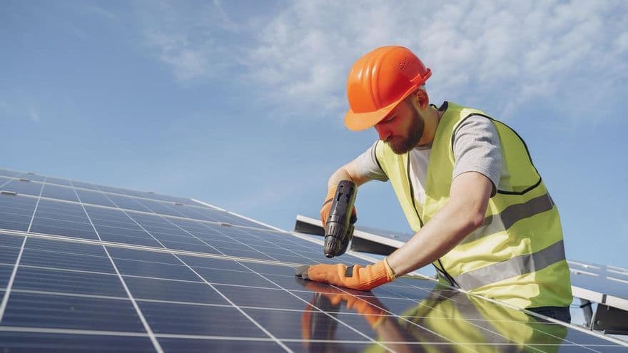 Worker installing solar panels on a rooftop, symbolizing sustainable practices for adapting to Spain's changing climate.